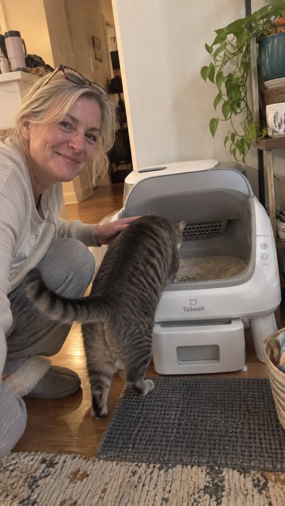 A Tailwell customer’s cat greeting them beside the self-cleaning litter box in the hallway